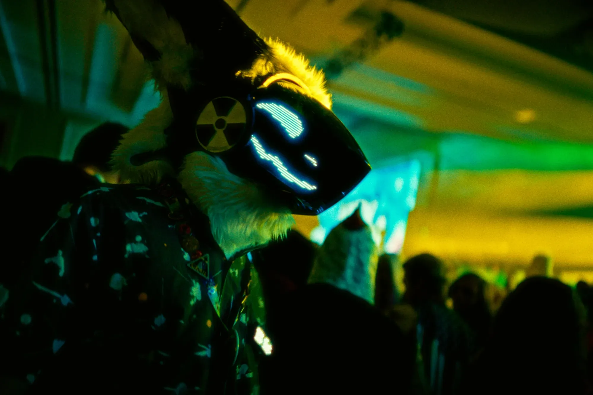 A fursuiter with a glowing LED visor mask on a green-and-yellow lit dance floor at Midwest FurFest.
