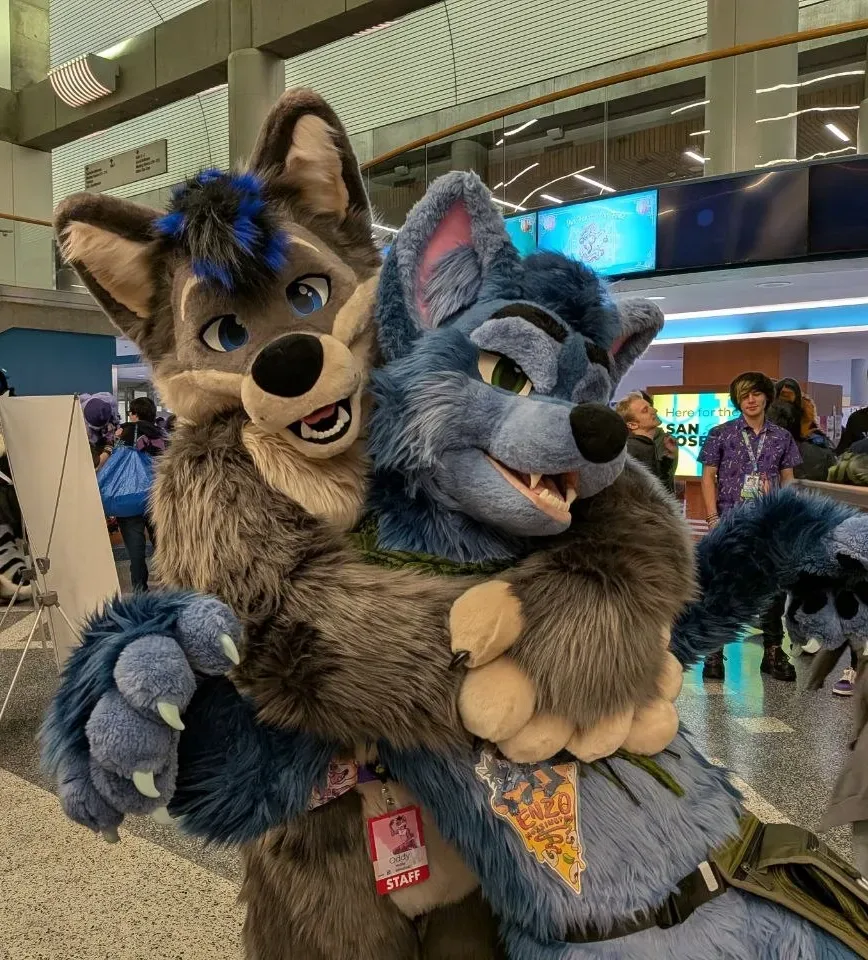 A pair of canine fursuiters embracing at Further Confusion 2026.